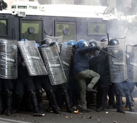 Policemen take shelter from bottles and flares thrown by demonstrators during a protest against austerity measures in downtown Rome