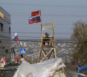 Pro-Russian protester watches through binoculars from lockout tower, with Russian and Belarussian national flags attached on it, near the seized office of the SBU state security service in Luhansk