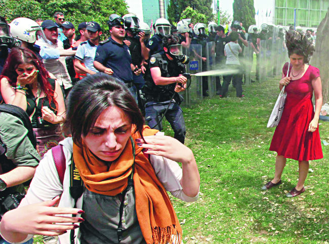Τρίτη 28 Μαΐου, πλατεία Ταξίμ. Η κοπέλα με το κόκκινο φόρεμα ψεκάζεται εν ψυχρώ με χημικά και γίνεται σύμβολο της τουρκικής νεολαίας, που τόλμησε να ορθώσει ανάστημα μπροστά στην παντοκρατορία Ερντογάν. Η φωτογραφία αυτή συμπύκνωσε την ουσία της εξέγερσης με αφορμή το πάρκο Γκεζί: την τυφλή βία των δυνάμεων ασφαλείας απέναντι σε ειρηνικούς διαδηλωτές, τον αυταρχισμό της εξουσίας απέναντι στη λαϊκή βούληση. Ο φωτορεπόρτερ του Reuters, Οσμάν Ορσάλ, που την τράβηξε, έπεσε κι αυτός θύμα της άγριας αστυνομικής καταστολής στην Πόλη, προσπαθώντας απλά να κάνει τη δουλειά του.
