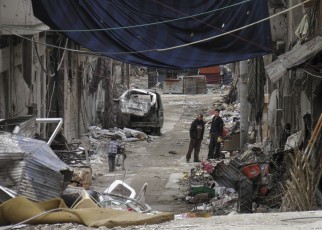 Residents stand along a damaged street filled with debris in the besieged area of Homs