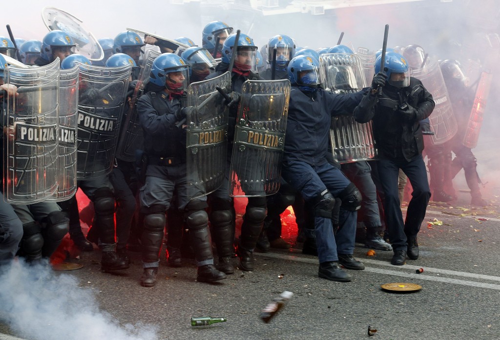 Policemen take shelter from bottles and flares thrown by demonstrators during a protest against austerity measures in downtown