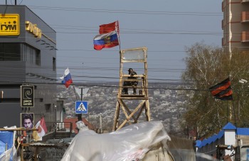 Pro-Russian protester watches through binoculars from lockout tower, with Russian and Belarussian national flags attached on it, near the seized office of the SBU state security service in Luhansk