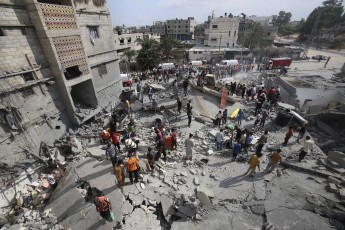Palestinian rescue workers search for victims as people gather atop the remains of a house in Khan Younis in the southern Gaza Strip