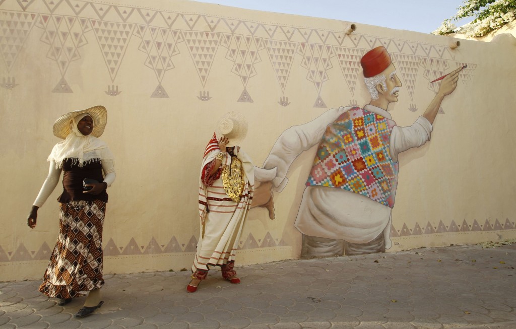 Women walk next to a mural by Portuguese artist Mario Belem in the village of Erriadh on Djerba